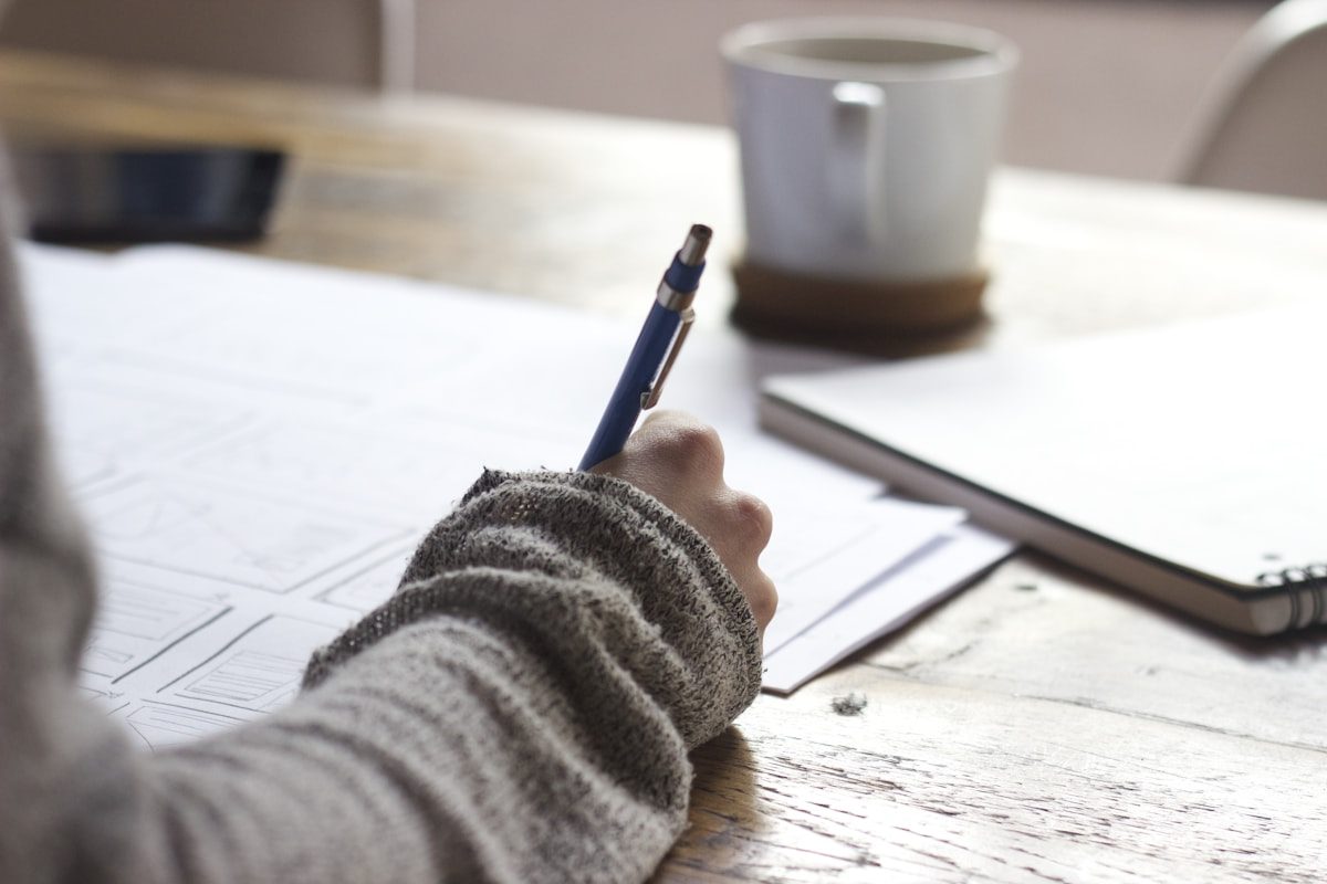 A person writing in a notebook at a wooden desk